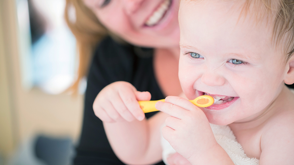 Baby in mother's lap brushing teeth