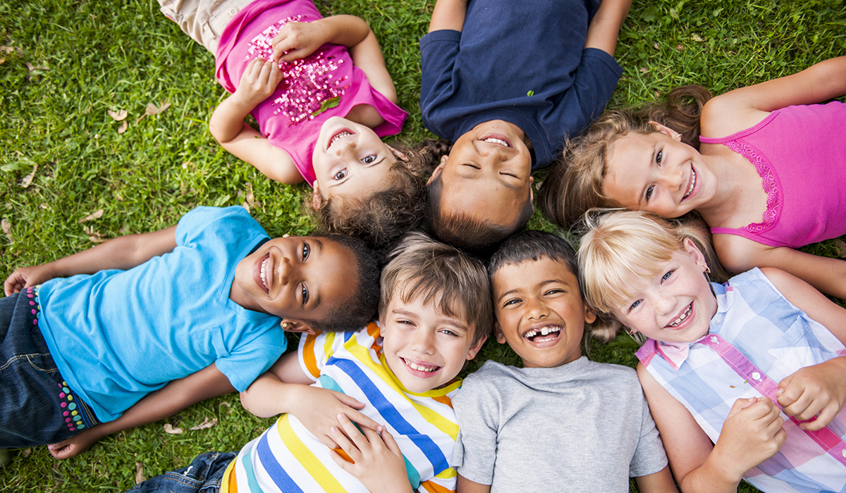 Children lying in a circle on the grass and enjoying summer fun with healthy smiles